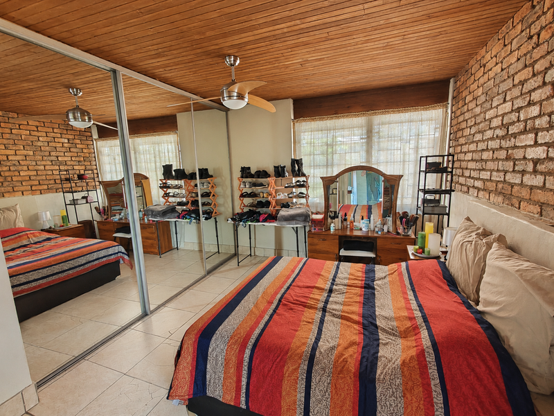 Spacious bedroom featuring exposed brick walls, a timber ceiling, tiled flooring, and large mirrored sliding wardrobes.