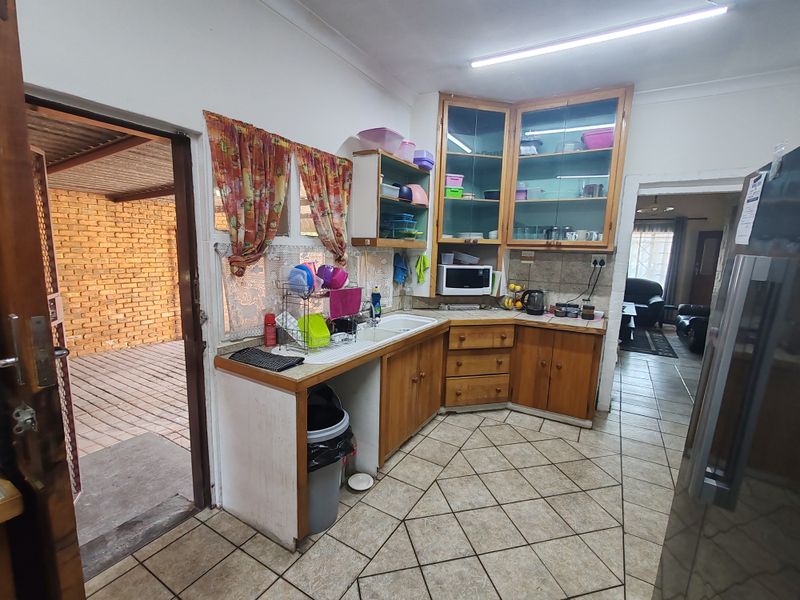 A functional kitchen featuring wooden cabinetry, laminate countertops, a double basin sink, and tiled flooring, with direct access to an outdoor patio area.