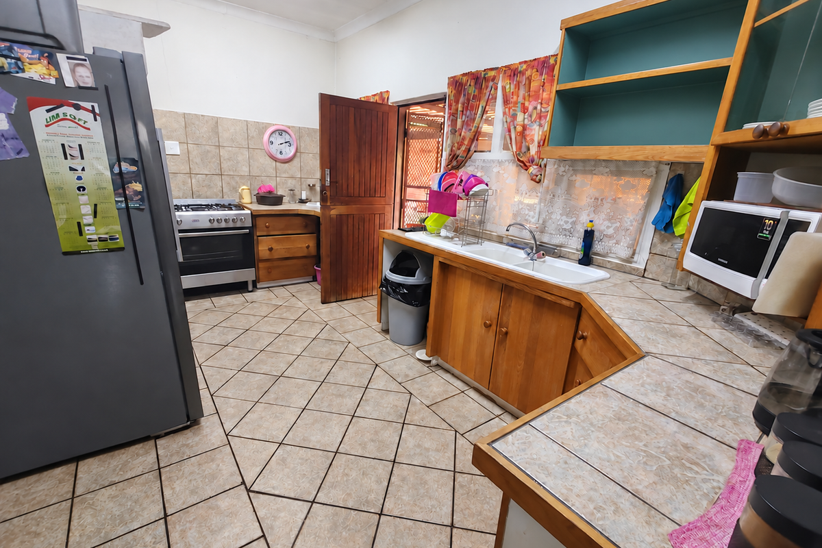 A functional kitchen featuring wooden cabinetry, a gas stove, double basin sink, and tiled flooring, offering potential for a modern renovation.