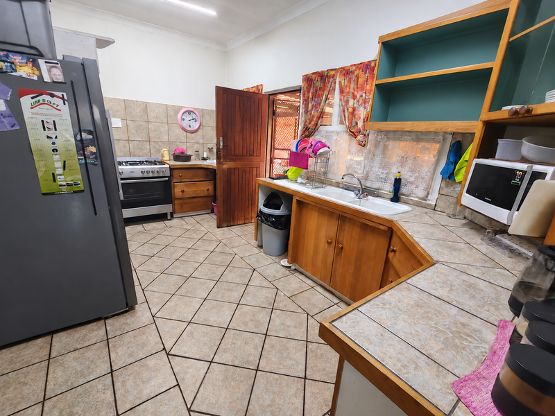 A functional kitchen featuring wooden cabinetry, a gas stove, double basin sink, and tiled flooring, offering potential for a modern renovation.