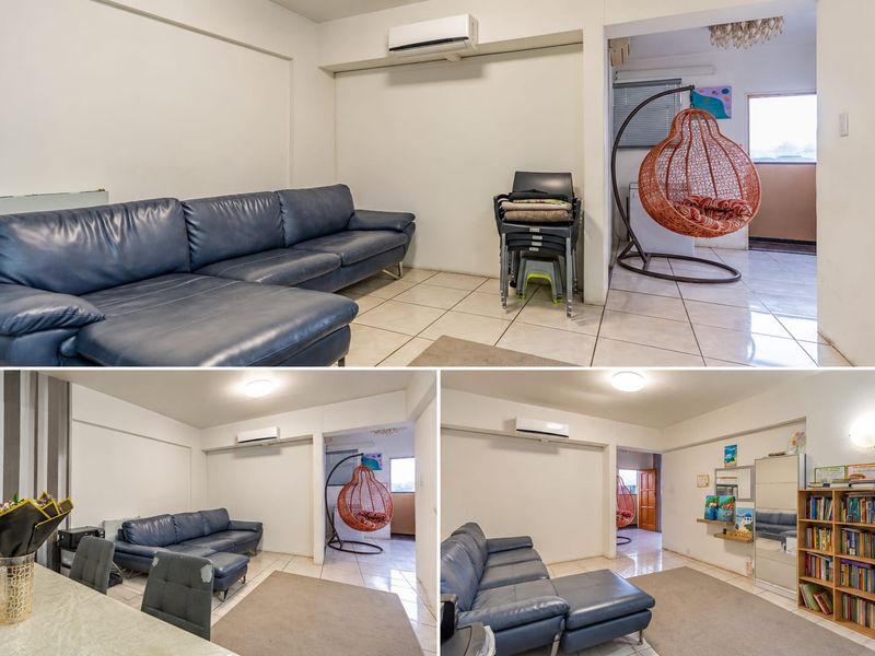 An open-plan living area featuring tiled flooring and a wall-mounted split-system air conditioner, connecting to an adjacent space.