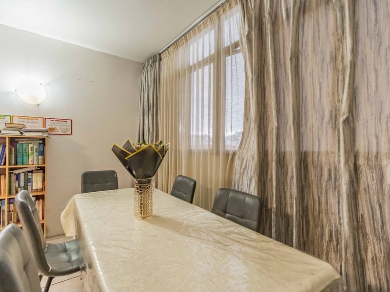 A dining room featuring a large window with floor-to-ceiling curtains and a wall-mounted light fixture.
