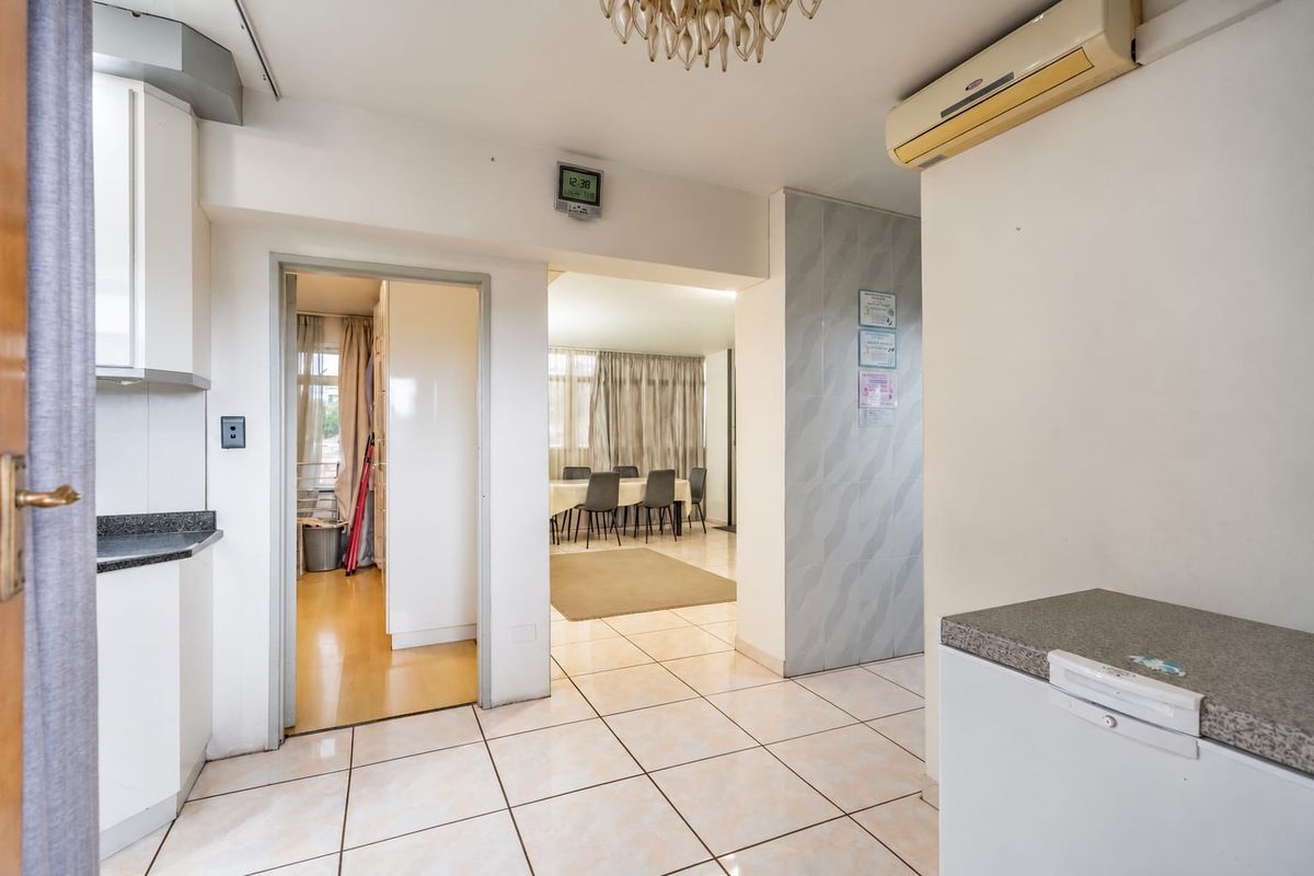 Open-plan living area featuring tiled flooring, built-in kitchen cabinetry with stone countertops, and a wall-mounted air conditioning unit.