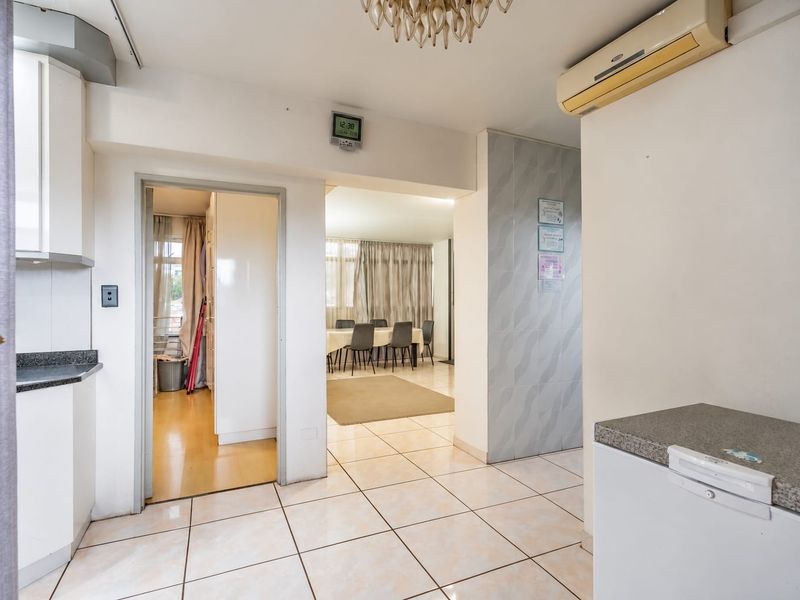Open-plan living area featuring tiled flooring, built-in kitchen cabinetry with stone countertops, and a wall-mounted air conditioning unit.