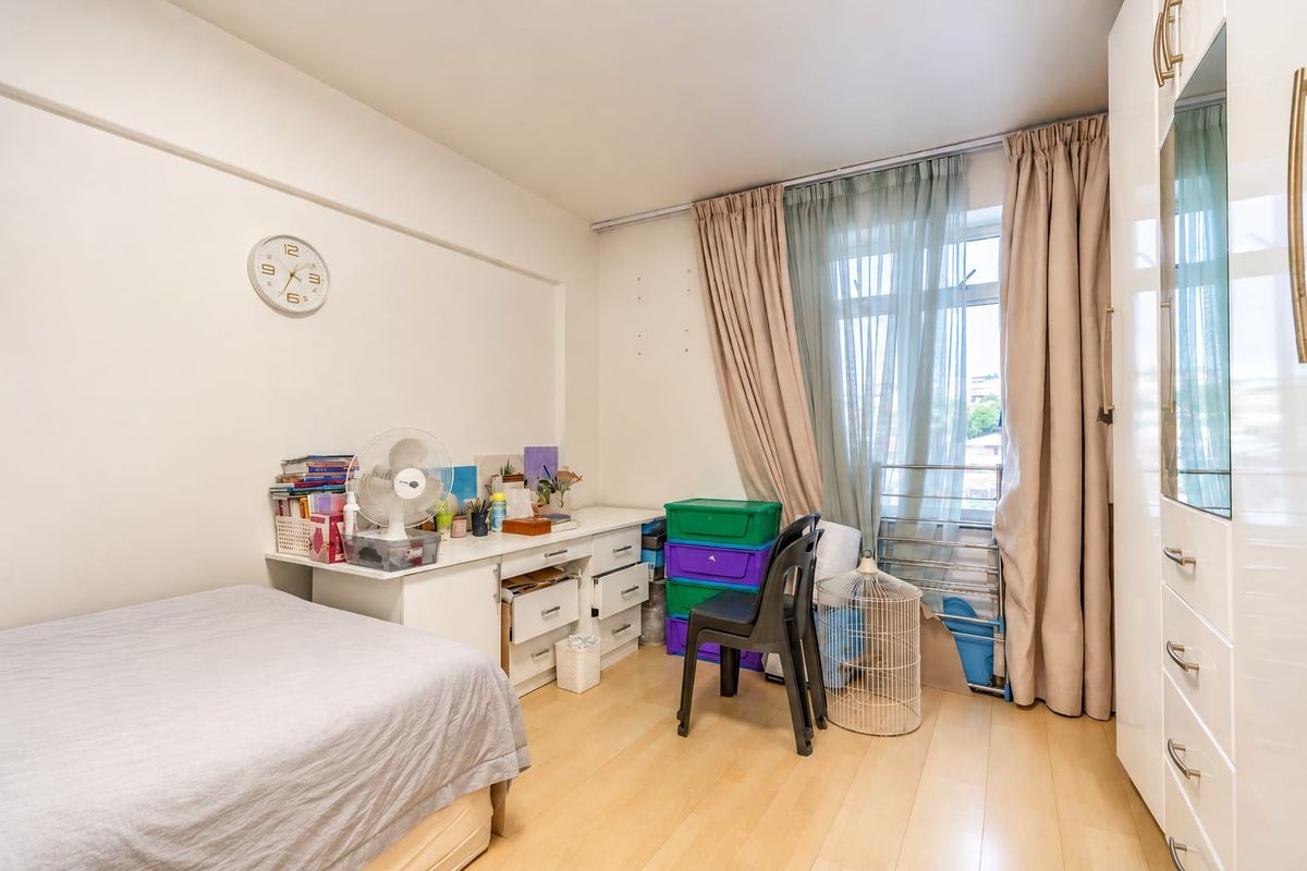 A bedroom featuring light-toned laminate flooring, a built-in wardrobe, and large windows with curtain tracks, offering a functional space with potential for updates.