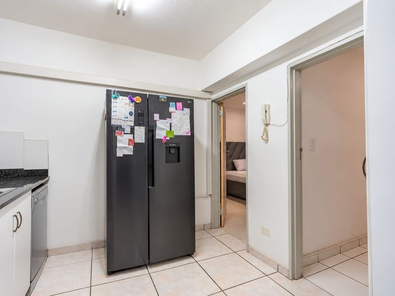 A functional kitchen area featuring tiled flooring, granite countertops, and a stainless steel sink, with direct access to adjacent rooms.