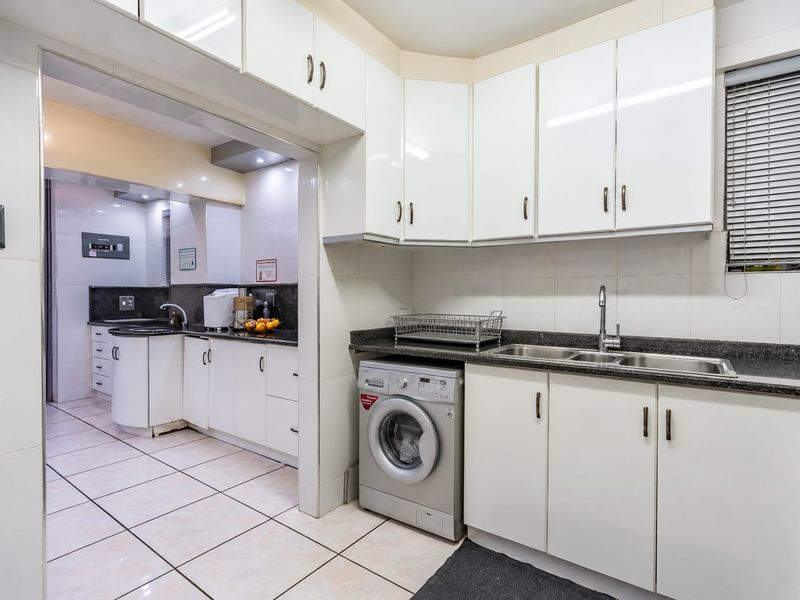 A functional kitchen featuring white cabinetry, granite countertops, a double basin sink, and an integrated washing machine with tiled flooring throughout.