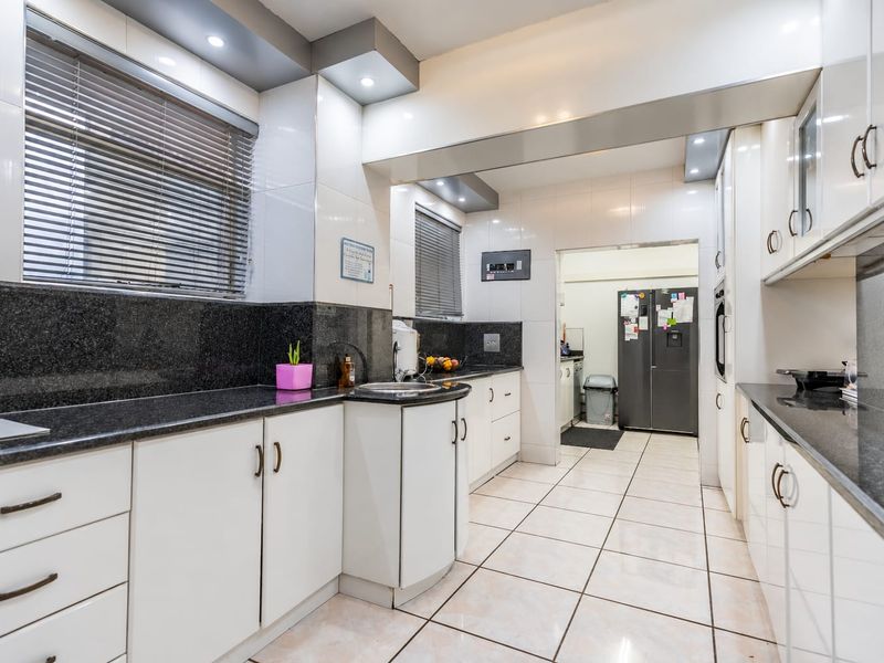 A well-maintained kitchen featuring white cabinetry, dark granite countertops, tiled flooring, and recessed lighting, with an adjacent scullery area.
