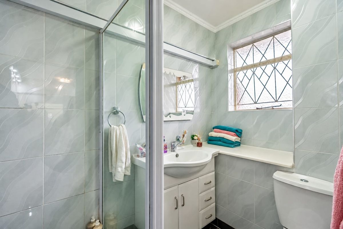 A functional bathroom featuring a shower enclosure, vanity cabinet with basin, toilet, and tiled walls with a decorative leaded glass window.