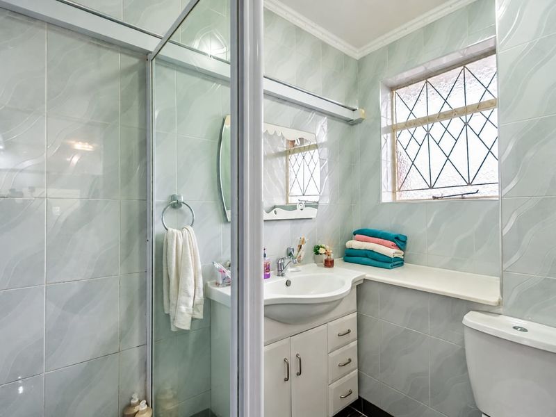 A functional bathroom featuring a shower enclosure, vanity cabinet with basin, toilet, and tiled walls with a decorative leaded glass window.