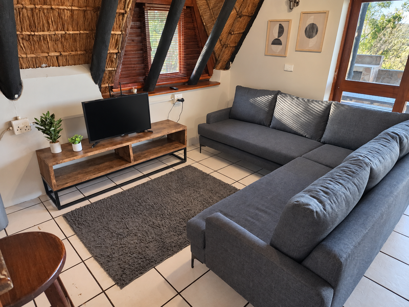 A cozy living room featuring a unique thatched roof with exposed timber rafters, tiled flooring, and direct access to an outdoor area.