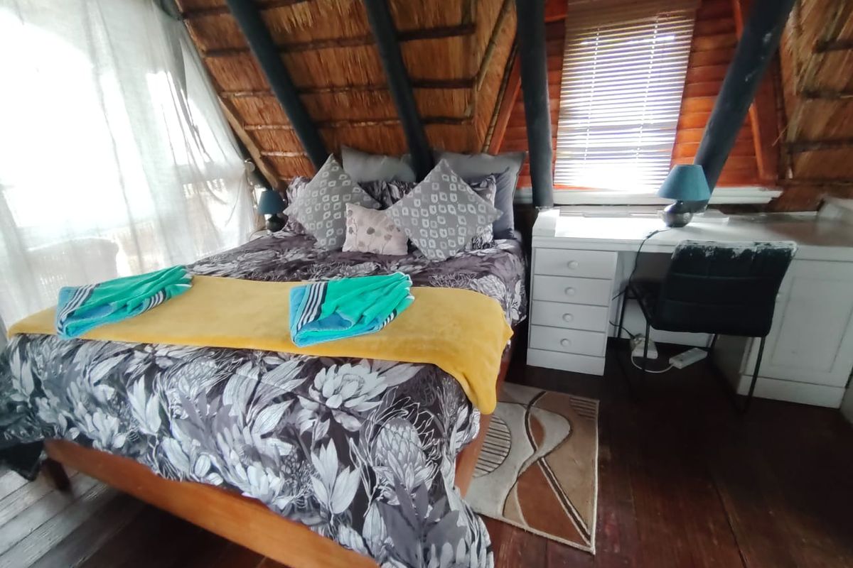Cozy bedroom featuring a unique thatched roof with exposed timber rafters, wooden flooring, and a built-in desk area.