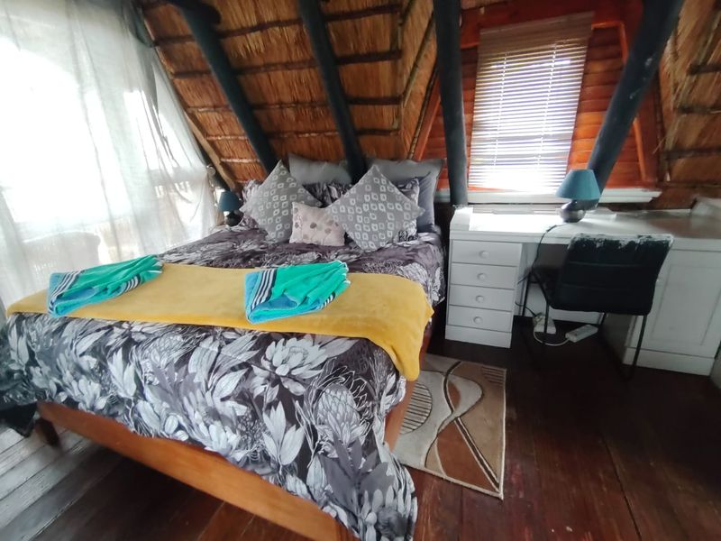 Cozy bedroom featuring a unique thatched roof with exposed timber rafters, wooden flooring, and a built-in desk area.