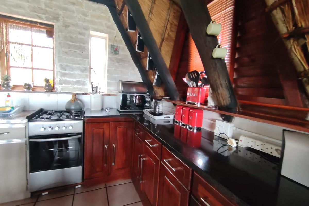 A rustic kitchen featuring dark wood cabinetry, granite countertops, a gas stove, and unique architectural elements including exposed timber rafters and a thatched ceiling.