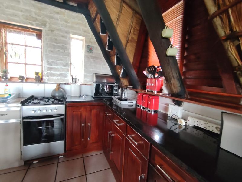 A rustic kitchen featuring dark wood cabinetry, granite countertops, a gas stove, and unique architectural elements including exposed timber rafters and a thatched ceiling.