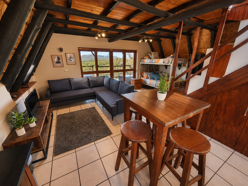 Open-plan living area featuring exposed timber beams, a thatched ceiling, tiled floors, and a wooden staircase leading to an upper level.