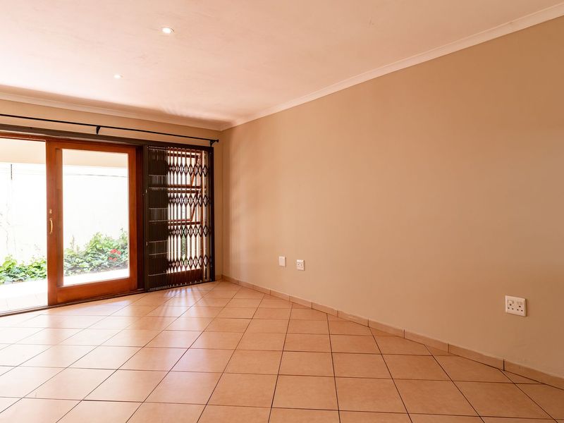 A bright, empty living area featuring neutral tiled flooring, recessed lighting, and a sliding glass door providing access to an outdoor space.