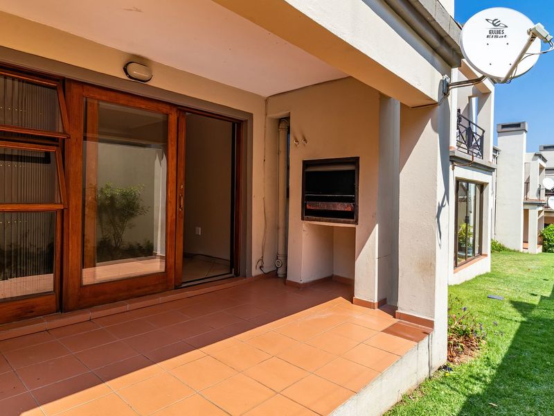 A covered patio featuring tiled flooring, a built-in braai, and wooden sliding doors providing access to the interior living space.