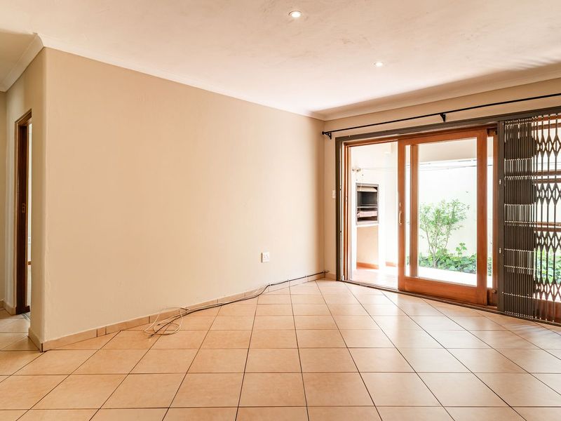 A bright, empty living room featuring tiled flooring, recessed lighting, and a sliding glass door with a security gate leading to an outdoor area.