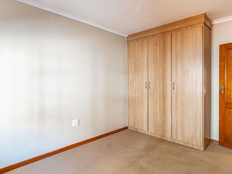 A clean, empty bedroom featuring neutral walls, fitted timber-finish wardrobes, and a solid wood door.