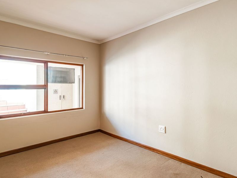 A clean, empty bedroom featuring neutral wall tones, carpeted flooring, and a timber-framed window with an installed curtain rod.