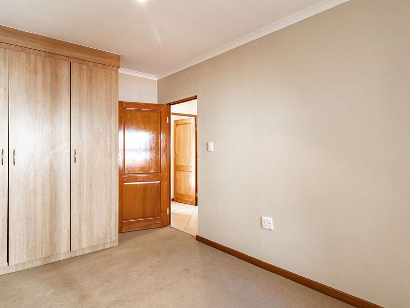 An empty bedroom featuring neutral walls, fitted light wood-finish wardrobes, and carpeted flooring, providing a blank canvas for personalization.