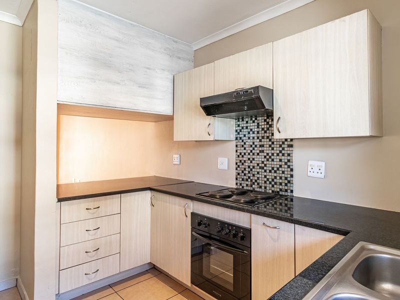 A functional kitchen featuring light wood-finish cabinetry, dark countertops, a built-in oven with hob, and a mosaic tile backsplash.