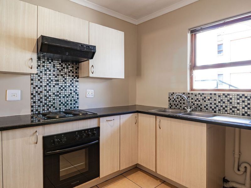 A functional kitchen featuring light wood-finish cabinetry, dark countertops, a mosaic tile backsplash, and integrated appliances including an oven and hob.