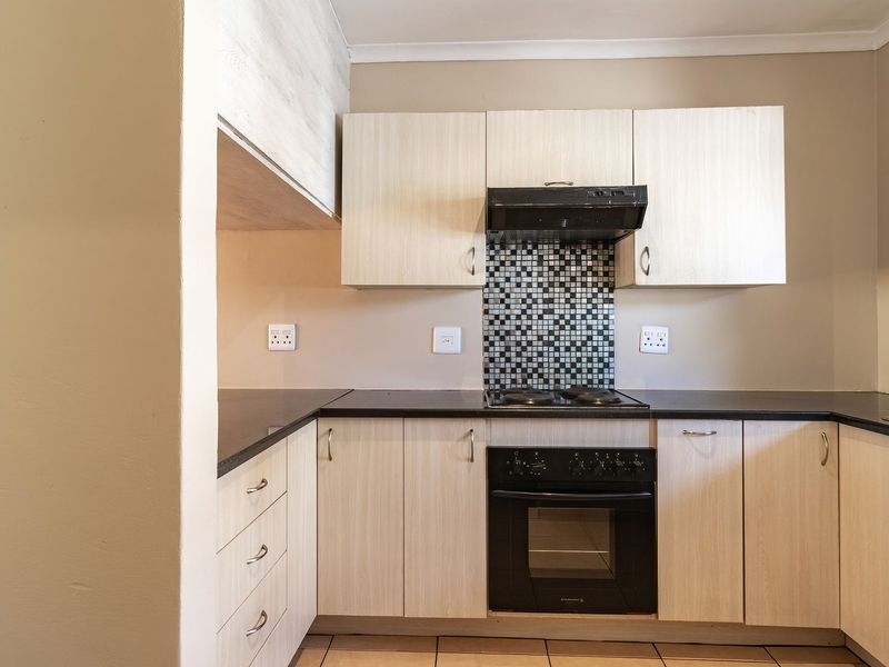 A functional kitchen featuring light wood-finish cabinetry, dark countertops, a mosaic tile backsplash, and integrated cooking appliances.