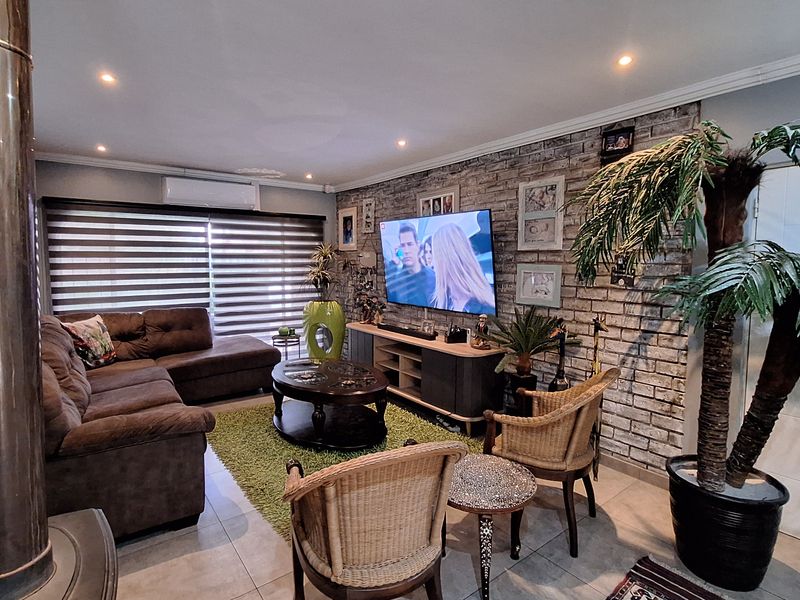 A comfortable living room featuring an exposed brick accent wall, tiled flooring, recessed lighting, and a built-in wood-burning fireplace.