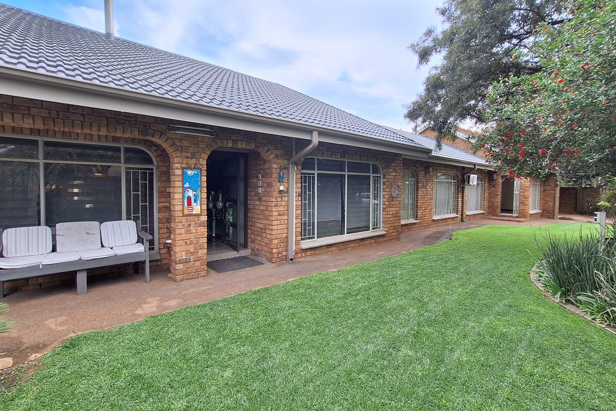 A well-maintained rear exterior view featuring a classic brick facade, tiled roof, paved patio area, and a neatly landscaped garden.