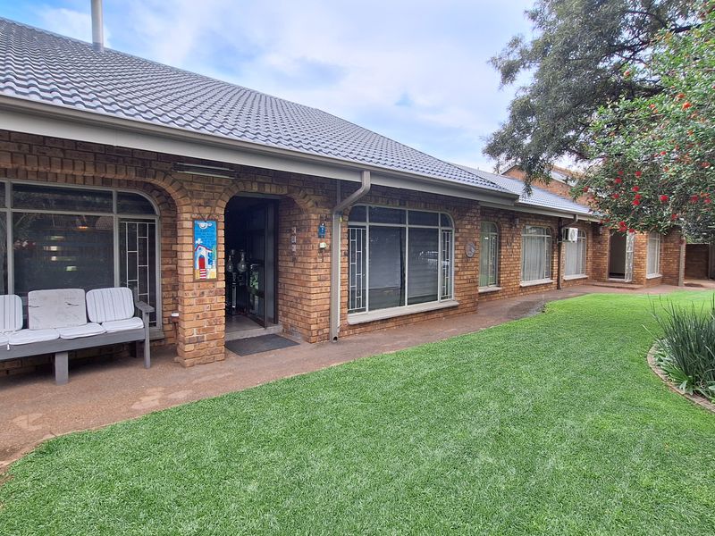 A well-maintained rear exterior view featuring a classic brick facade, tiled roof, paved patio area, and a neatly landscaped garden.