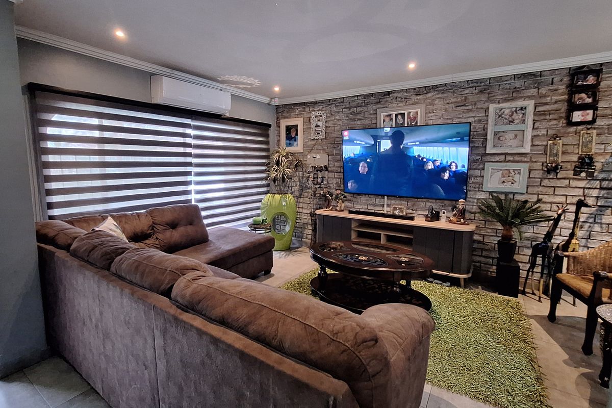 A comfortable living room featuring an exposed brick accent wall, recessed downlighting, and a wall-mounted air conditioning unit.