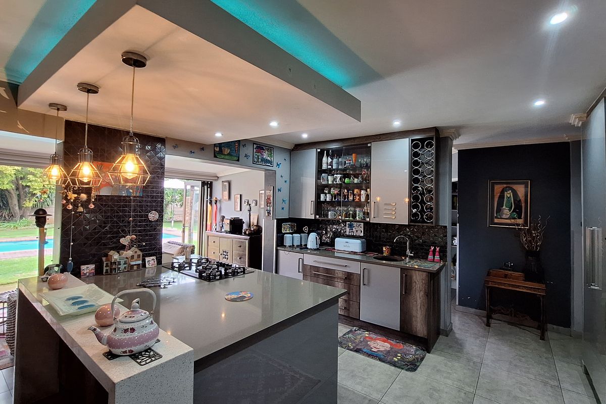 Modern kitchen featuring a large island with gas hob, stone countertops, integrated wine storage, and stylish pendant lighting overlooking the garden.