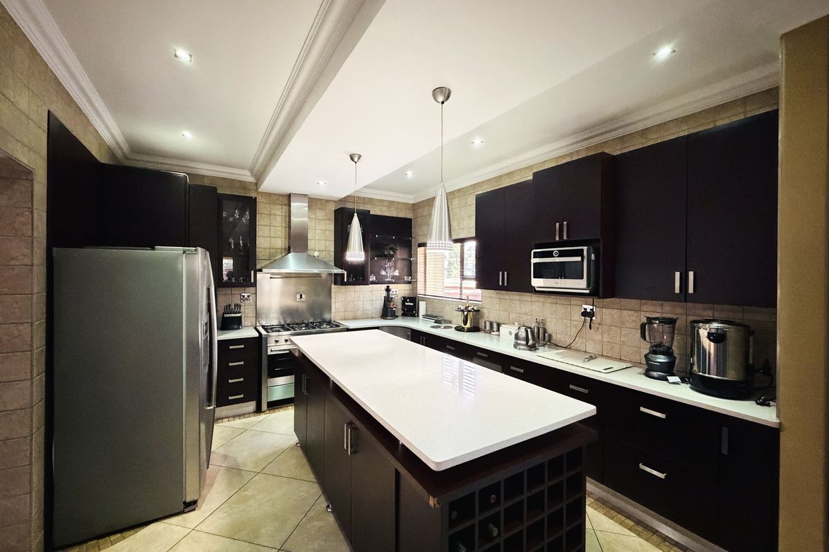 Modern kitchen featuring dark cabinetry, a central island with stone countertops, integrated appliances, and a gas hob with a stainless steel extractor fan.