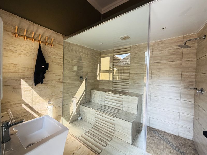 Modern bathroom featuring a spacious walk-in shower with a glass enclosure, built-in tiled bench, rain shower head, and contemporary neutral wall tiling.
