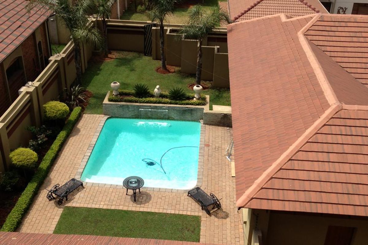 Aerial view of a residential property featuring a swimming pool, paved patio area, and landscaped garden surrounded by boundary walls.