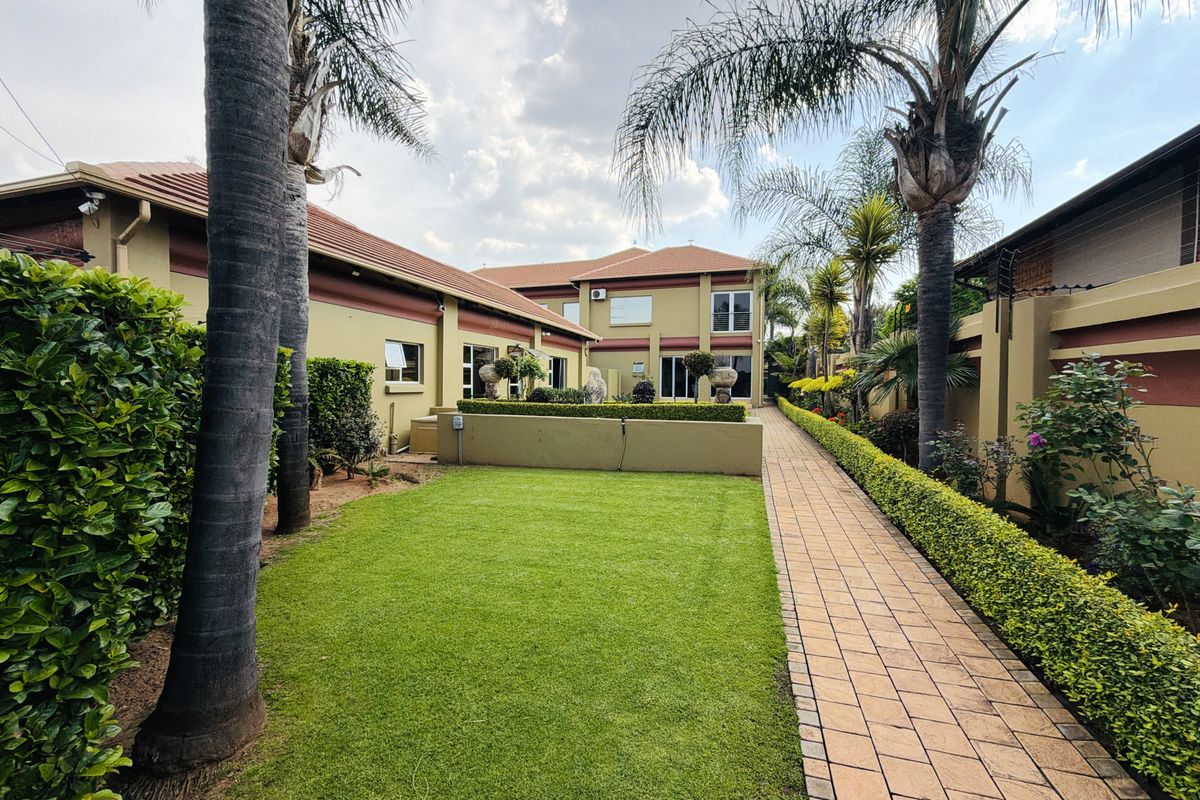 A well-maintained rear garden featuring a paved walkway, manicured lawn, and established landscaping alongside the property's exterior facade.