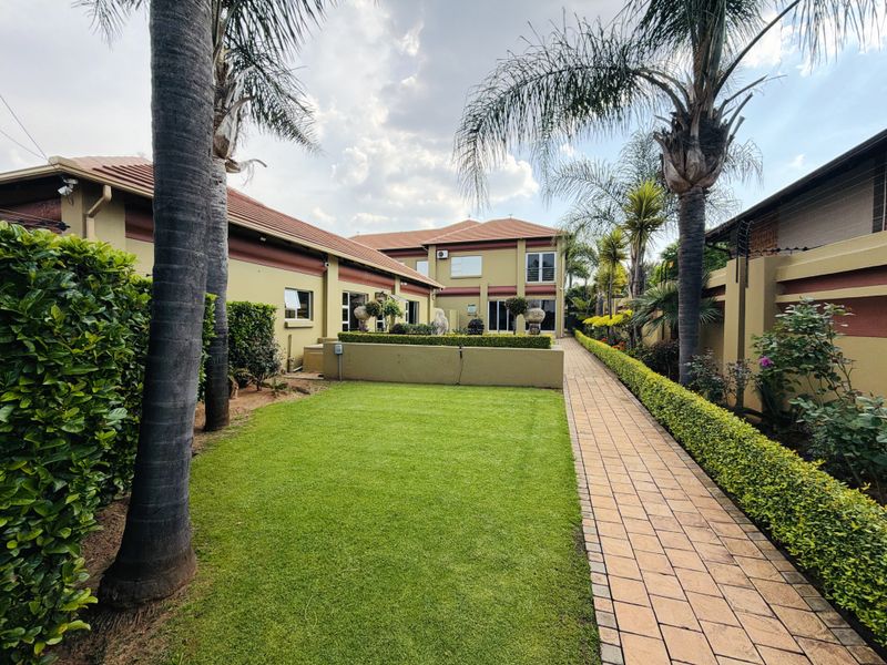 A well-maintained rear garden featuring a paved walkway, manicured lawn, and established landscaping alongside the property's exterior facade.