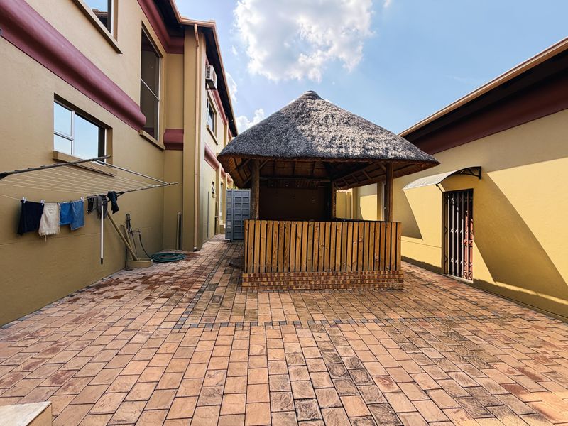Rear courtyard featuring a thatched gazebo and brick paving, providing an outdoor entertainment space between the main building structures.