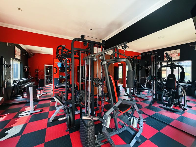 A dedicated home gym space featuring high-contrast red and black rubberized flooring, mirrored walls, and integrated recessed lighting.