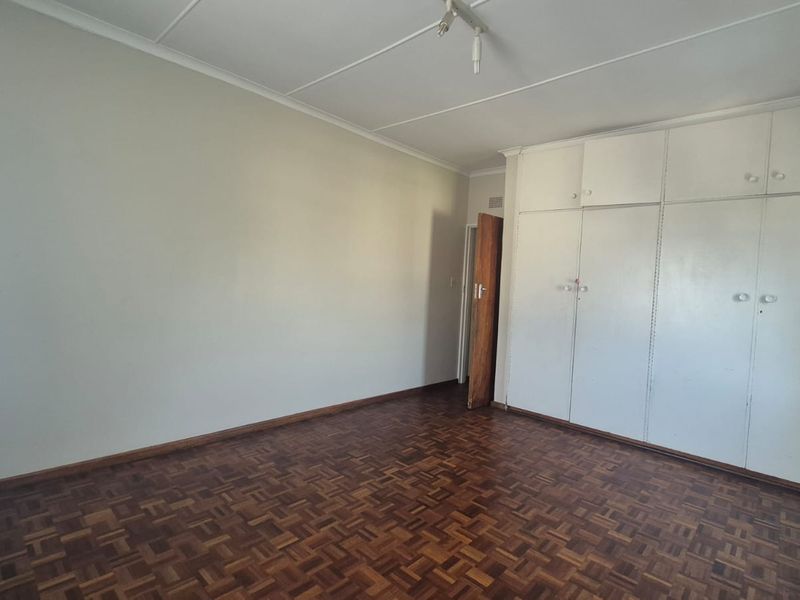 An empty bedroom featuring classic parquet flooring and extensive built-in cupboard storage, offering a blank canvas for personalization.