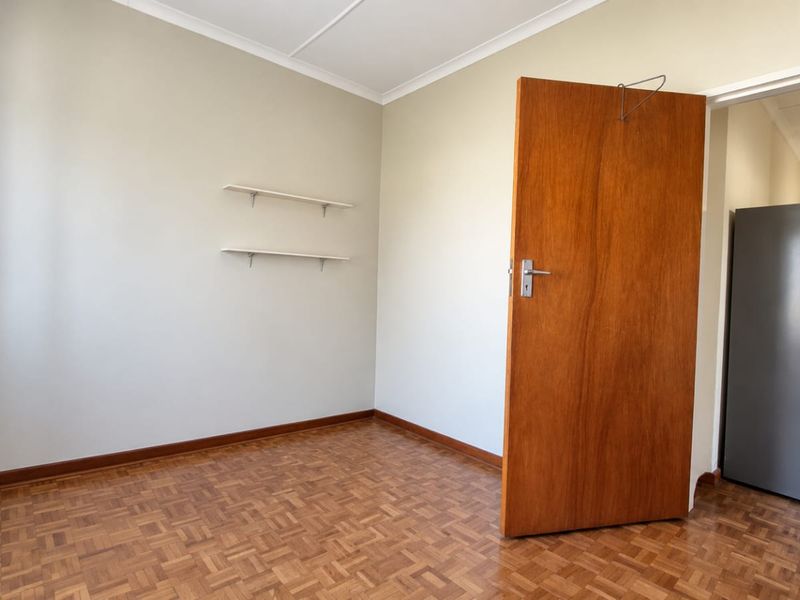 An empty bedroom featuring classic parquet flooring, neutral wall tones, and a solid wooden door, offering a clean canvas for personalization.