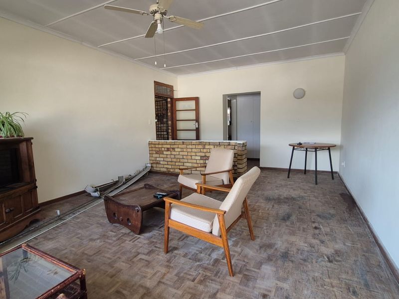 Spacious living area featuring original parquet flooring, a ceiling fan, and a decorative exposed brick partition wall.