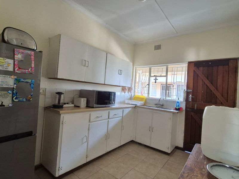 A functional kitchen featuring white built-in cabinetry, laminate countertops, and tiled flooring, offering a practical layout with potential for modern updates.