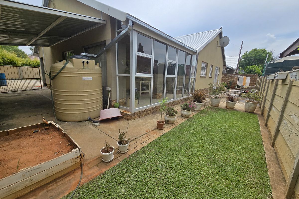 Rear exterior view featuring a lawn, paved area, enclosed patio, and a large water storage tank against the side of the house.