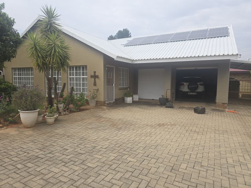 Front elevation of a residential house featuring a paved driveway, double garage, and roof-mounted solar panels.