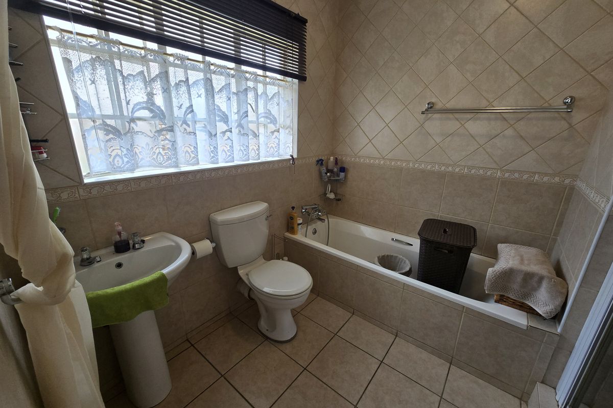A functional bathroom featuring a pedestal basin, toilet, and built-in bathtub with neutral ceramic wall and floor tiling.