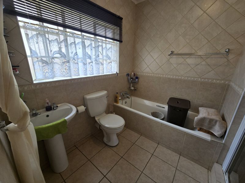 A functional bathroom featuring a pedestal basin, toilet, and built-in bathtub with neutral ceramic wall and floor tiling.
