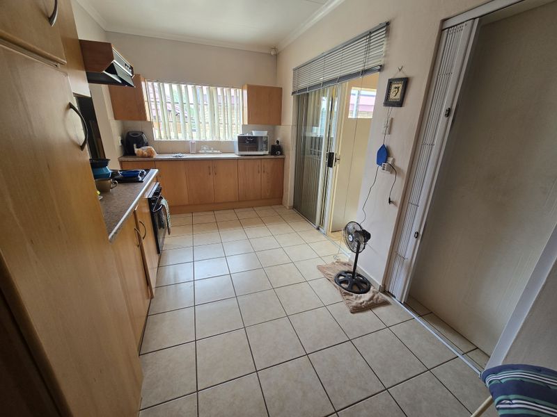 A functional kitchen featuring wood-finish cabinetry, laminate countertops, and ceramic tile flooring, with direct access to an outdoor area via a sliding glass door.